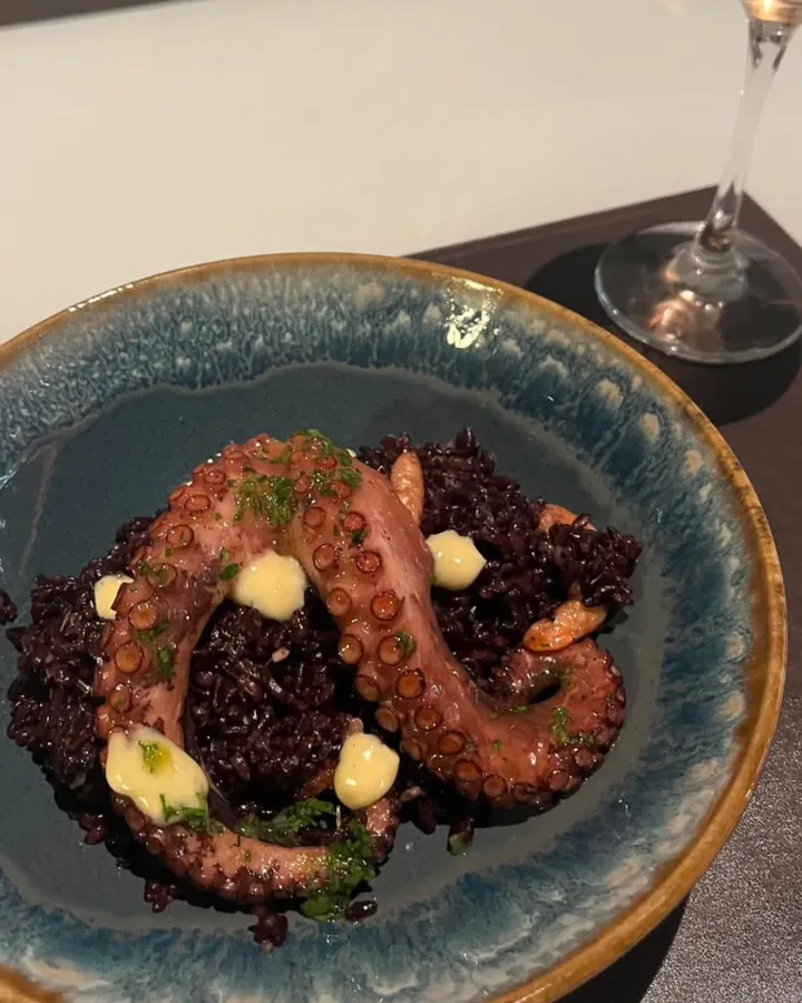 Arroz negro com polvo grelhado servido em prato de cerâmica, preparado pela Chef Angie